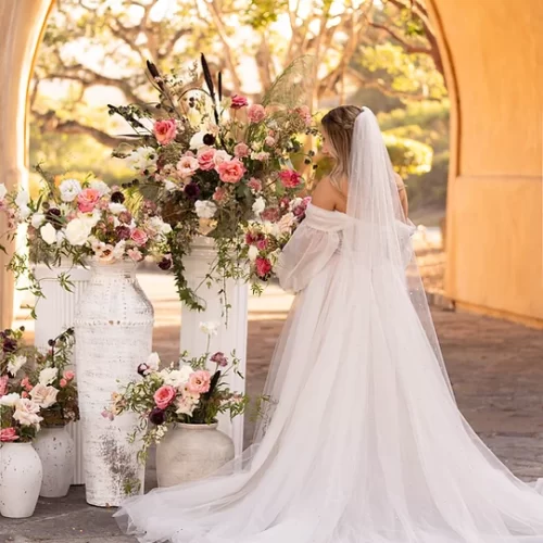 photo of bride in her dress in front of a large vase of flowers.